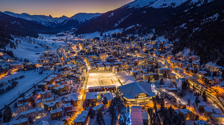 Night aerial view of Davos under snow with lit streets and the outdoor ice rink glowing in the town centre