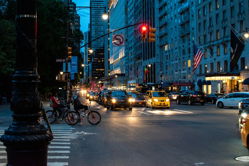 pessoas andando no caminho perto de edifícios da cidade e diferentes veículos na estrada durante a noite