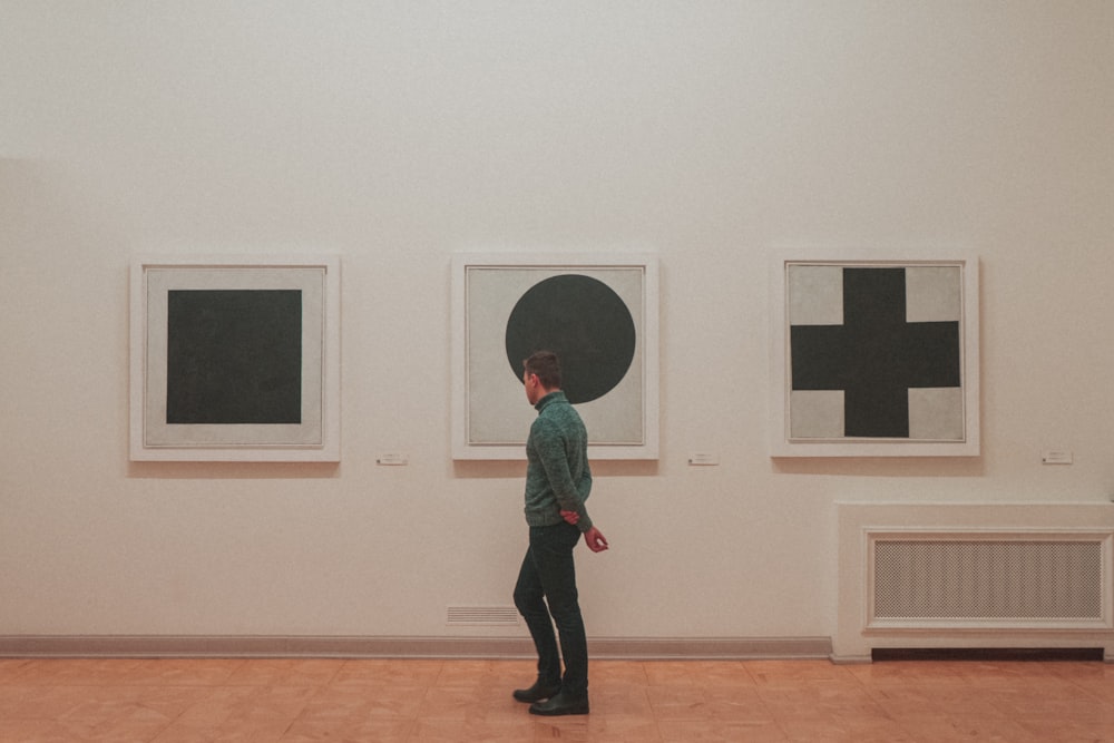 man wearing gray long-sleeved shirt standing near circle art inside building