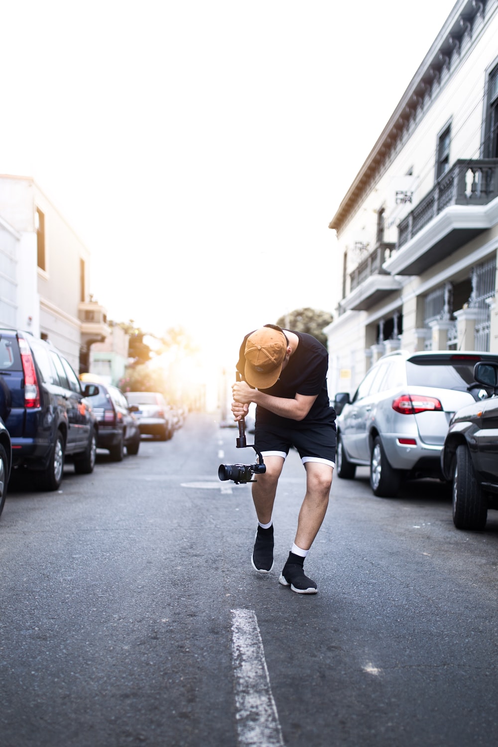 man wearing black crew-neck t-shirt holding video camera while walking and taking video on street