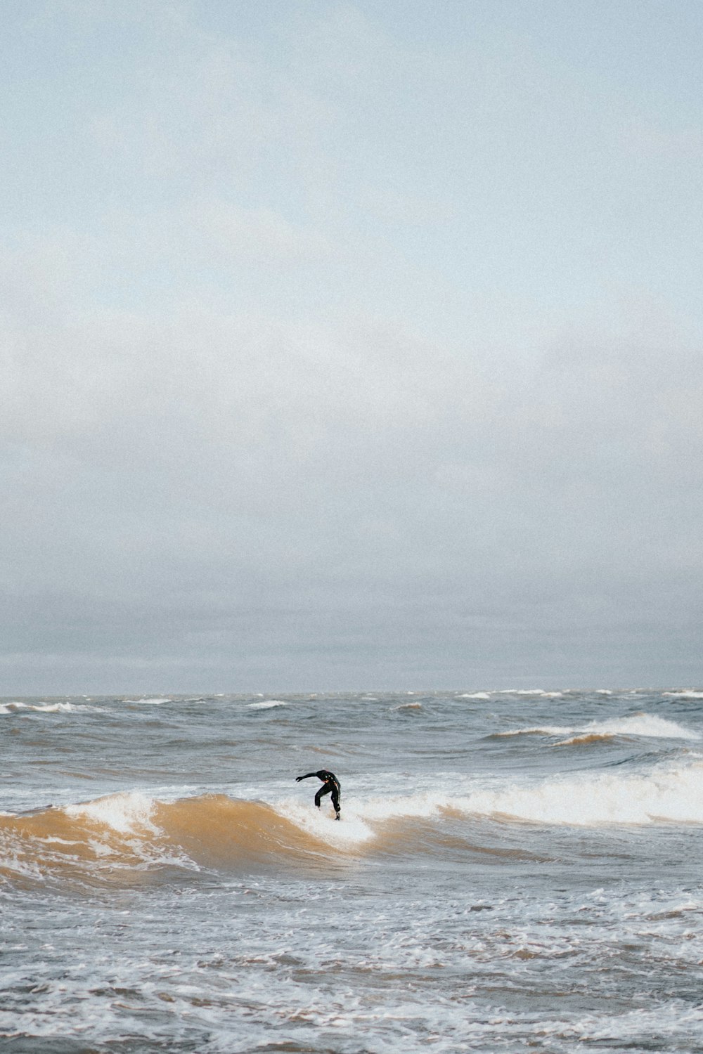 Persona che fa surf sull'onda del mare sotto il cielo bianco