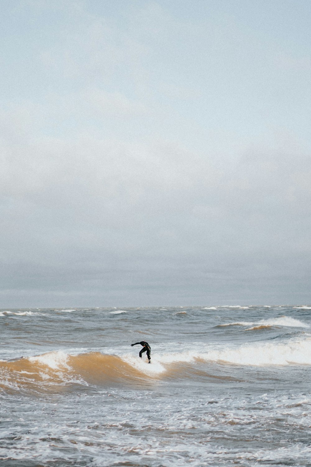 Person, die auf Meereswelle unter weißem Himmel surft