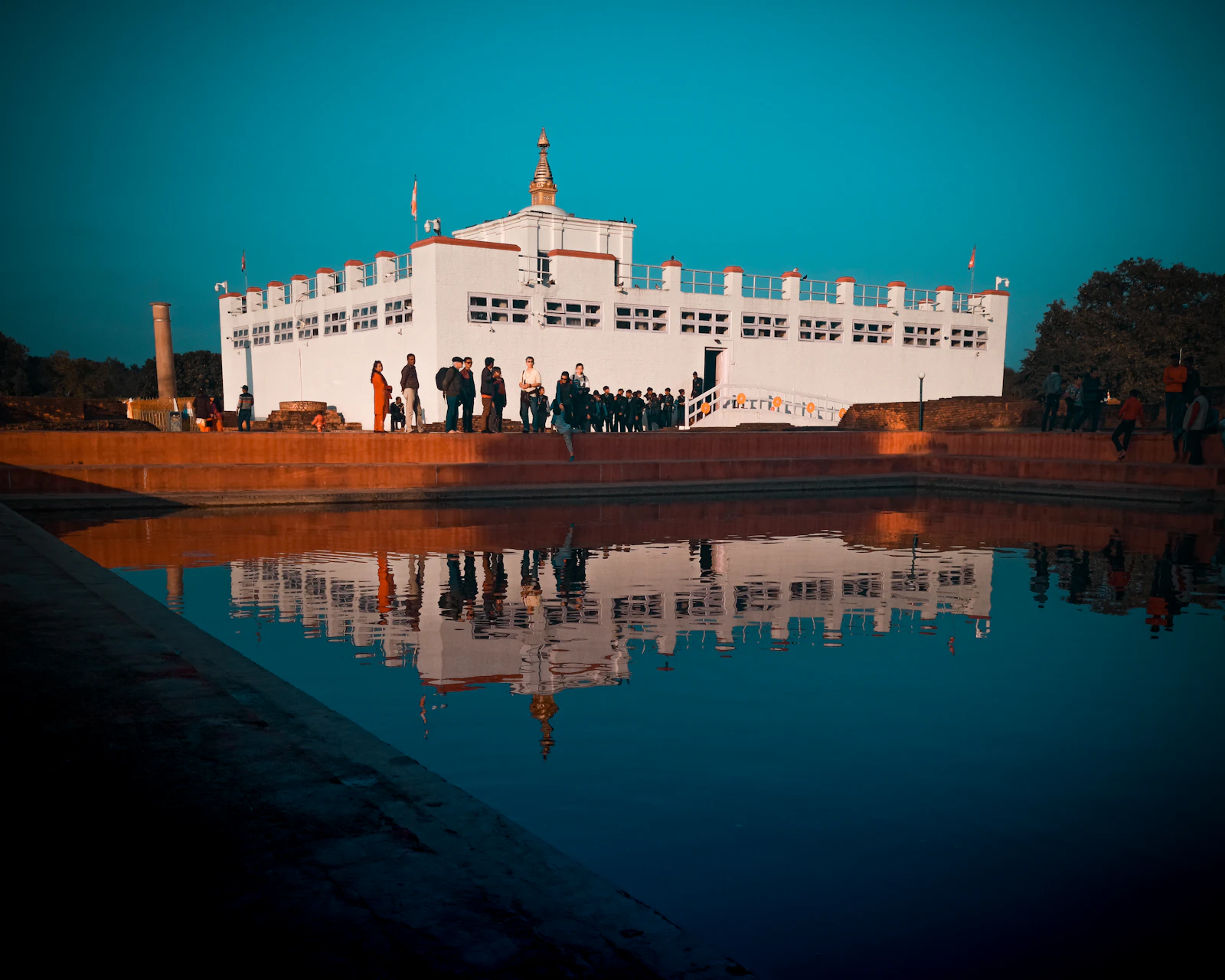 The Maya Devi Temple at Lumbini reflected in the Puskarini pond in low sun, the Ashoka pillar at the left edge
