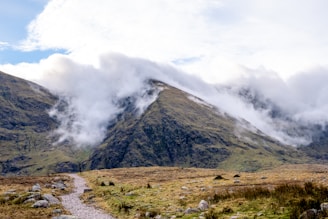 A winding trail through misty Scottish Highlands with rugged hills in the background.