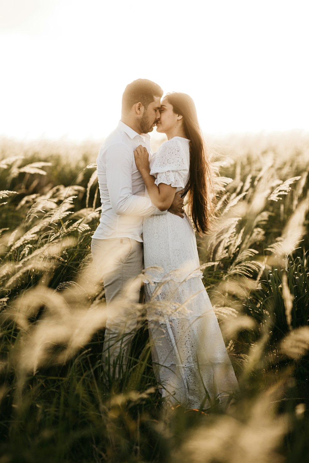 man and woman standing while facing each other and about to kiss on lips near green field