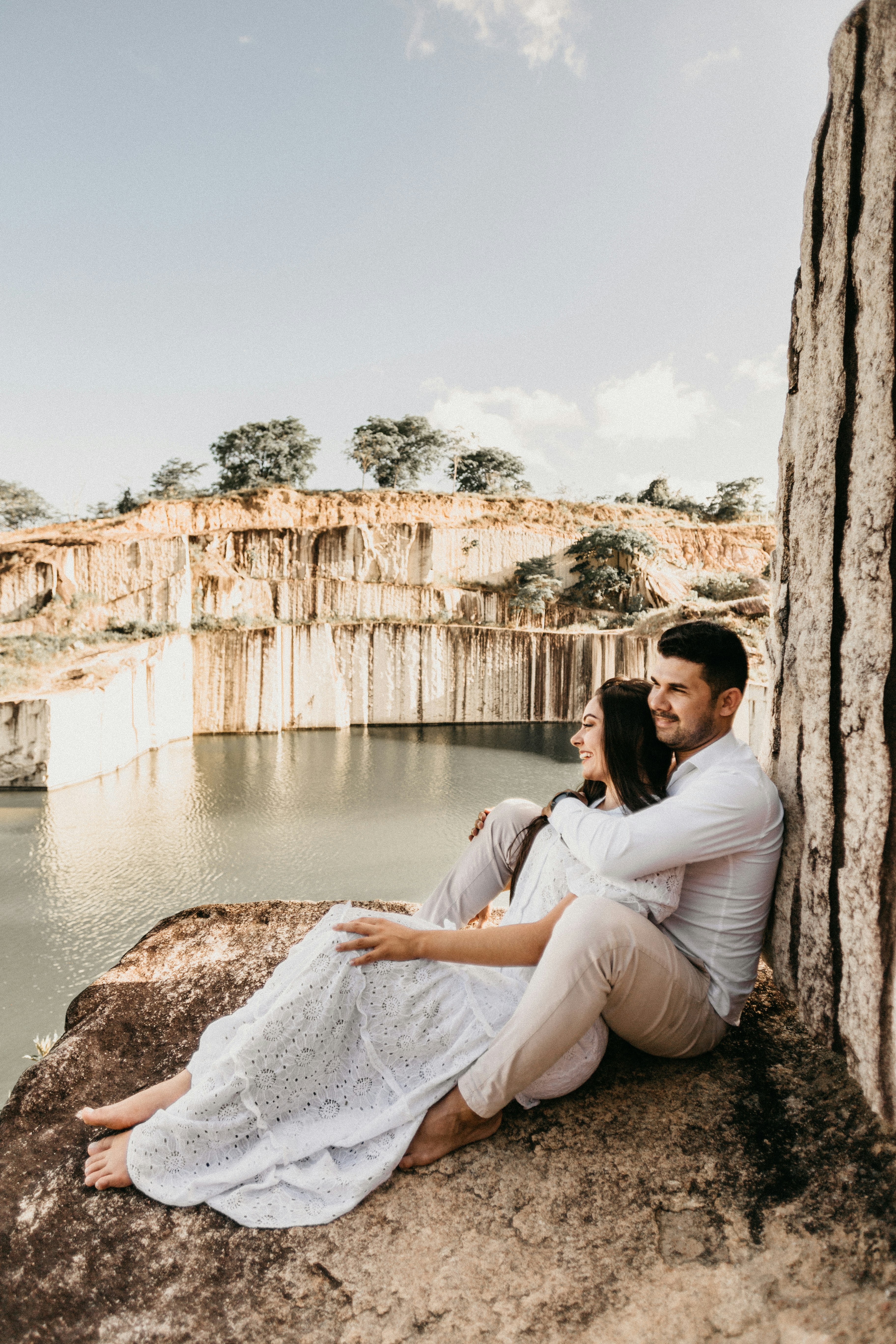 smiling man and woman sitting on rock near body of water during daytime