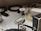 A workspace with a focus on a soldering setup where a helping hand tool is holding a wire. The wire has exposed ends and is positioned in front of a magnifying glass. In the background, various spools, cables, and electronic components are spread on the table.