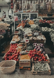 A vibrant crate overflowing with fresh green leafy vegetables and colorful fruits, set against a rustic wooden market stall backdrop.