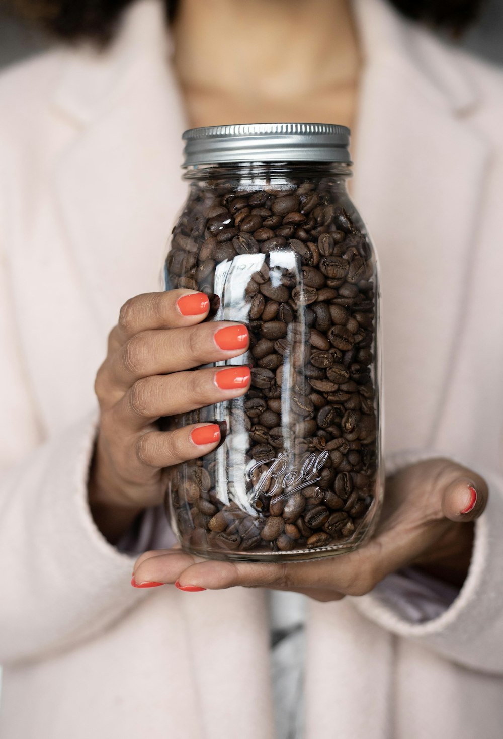Persona sosteniendo frasco de vidrio transparente con granos de café
