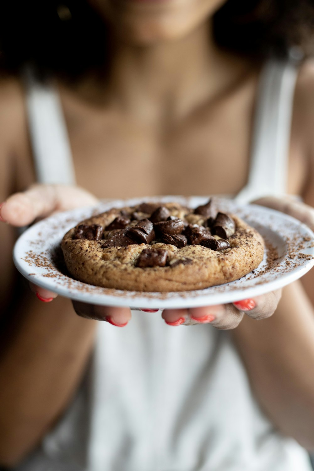 woman holding white saucer with cookie on top