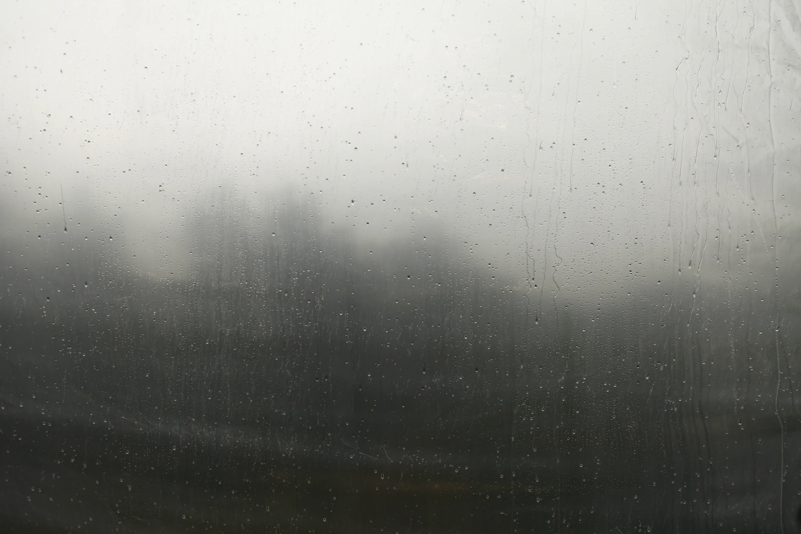 A window streaked with rain drops, representing the sessions referrer-based AI tracking can't see clearly: real AI-driven visits that arrive with no referrer for GA4 to match against