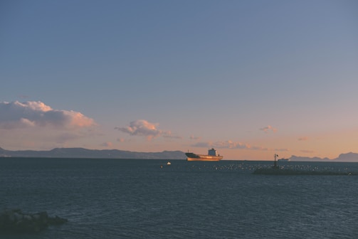 A sleek cargo ship sailing under a clear blue sky at dawn