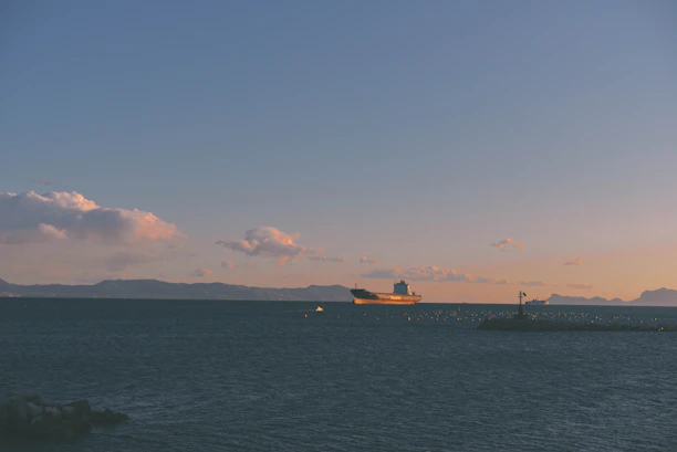 A large cargo ship navigating calm seas under a clear sky at sunset.