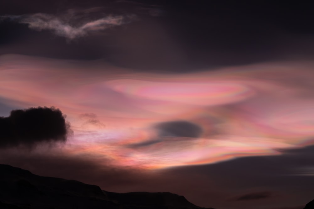 a very colorful cloud in the sky above a mountain