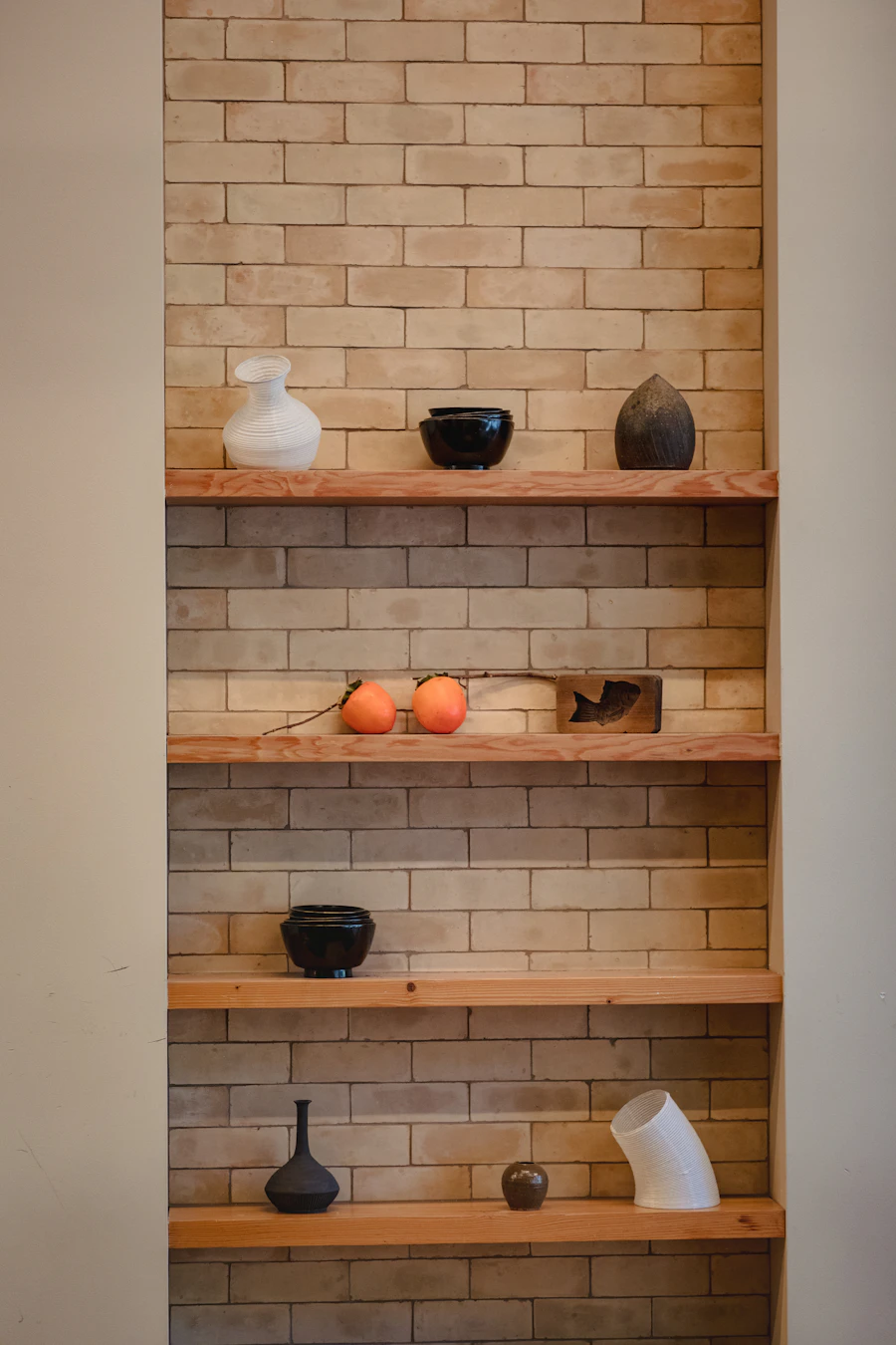 Wooden floating shelves with vases and bowls in a brick alcove