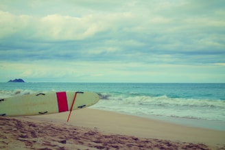 A vibrant surfboard leaning against a sandy beach with gentle waves in the background.
