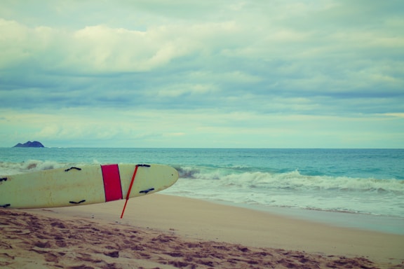 A vibrant surfboard leaning against a sandy beach with gentle waves in the background.