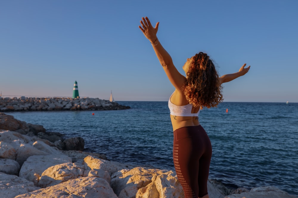 Mujer con sujetador deportivo blanco y pantalones negros de pie en la orilla del mar