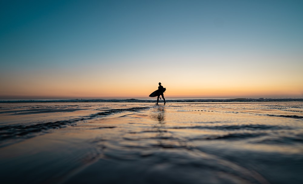 Persona in piedi sulla riva del mare tenendo la tavola da surf