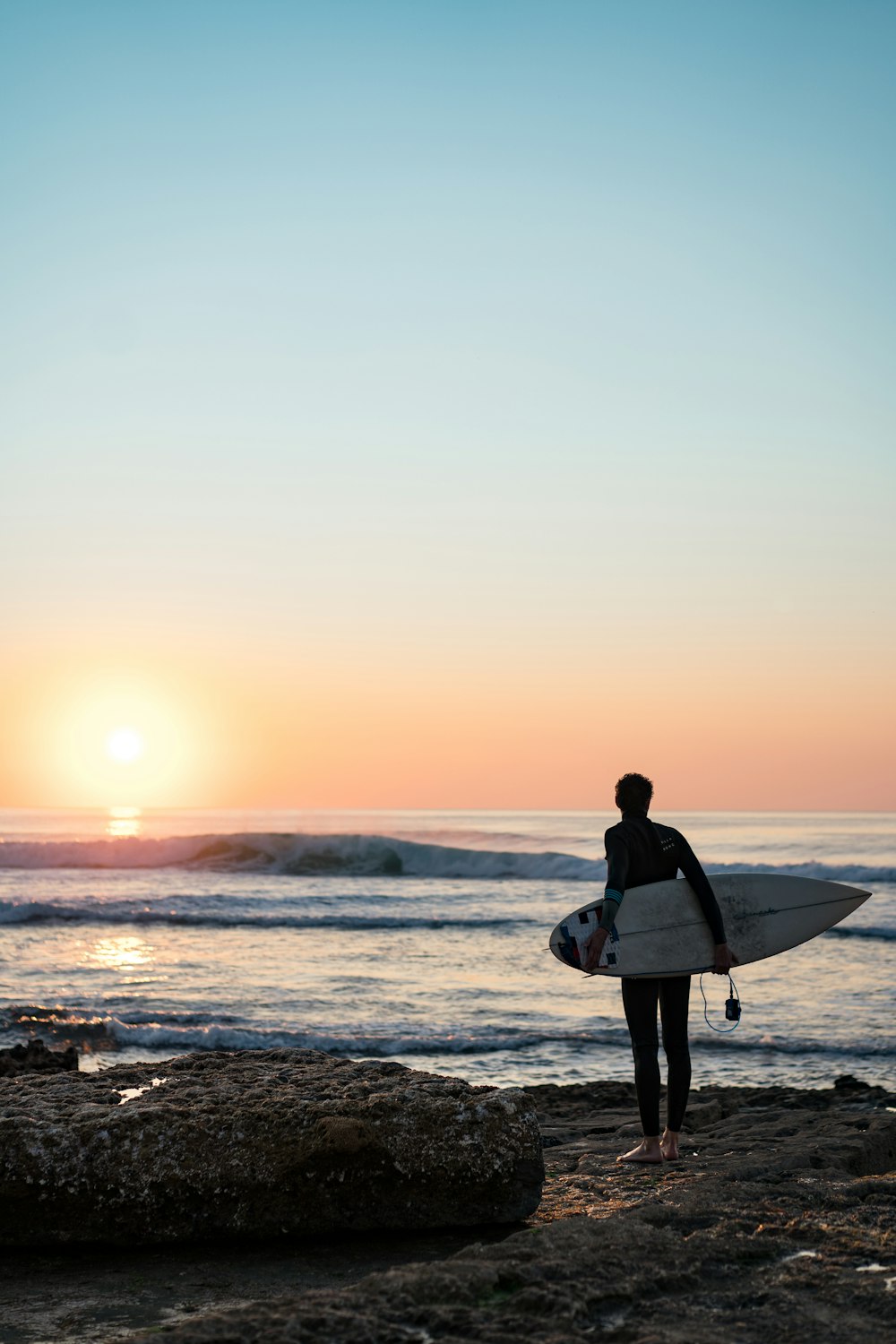 eine Person, die an einem Strand steht und ein Surfbrett hält