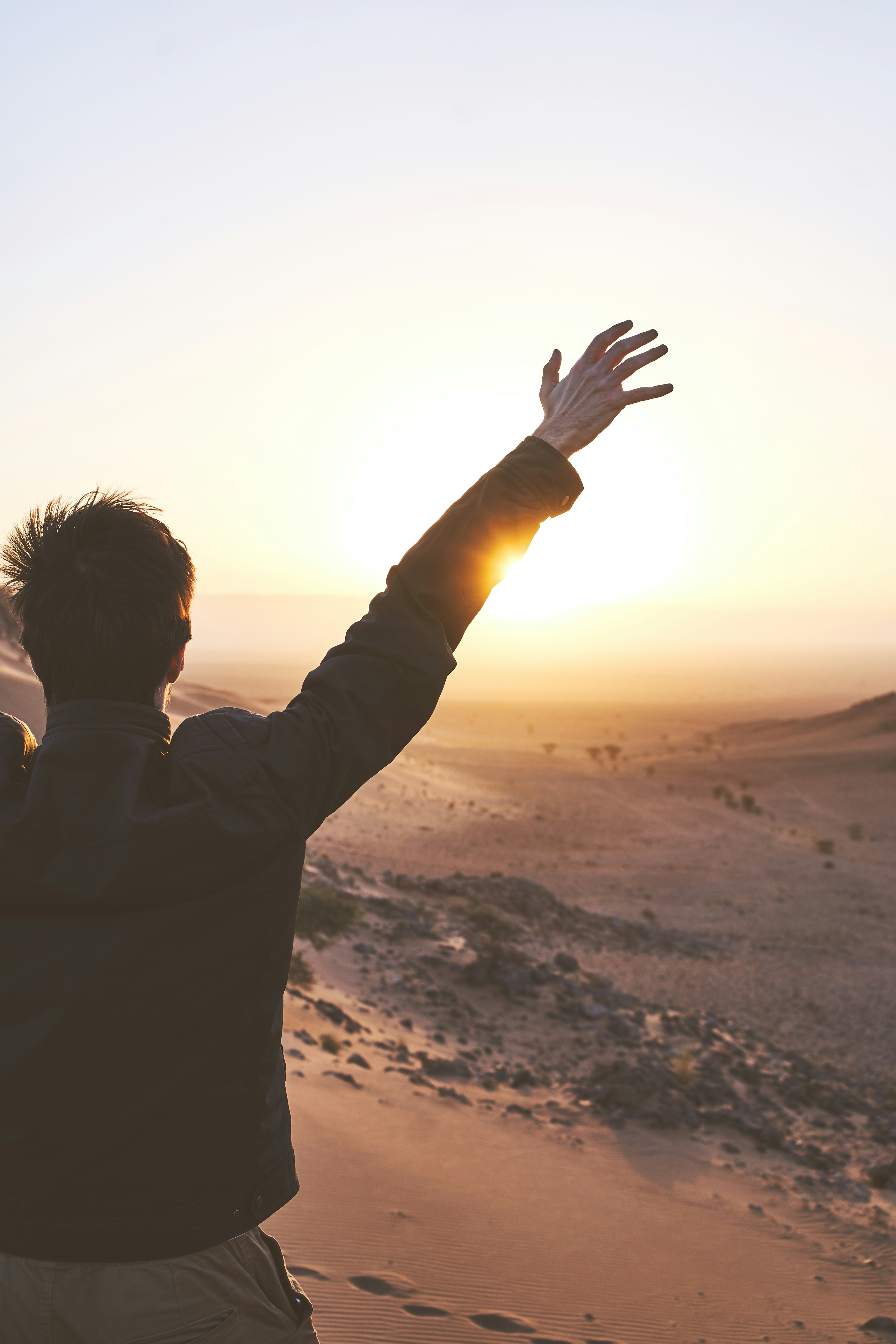 A man holding arms up in a desert on a sunrise