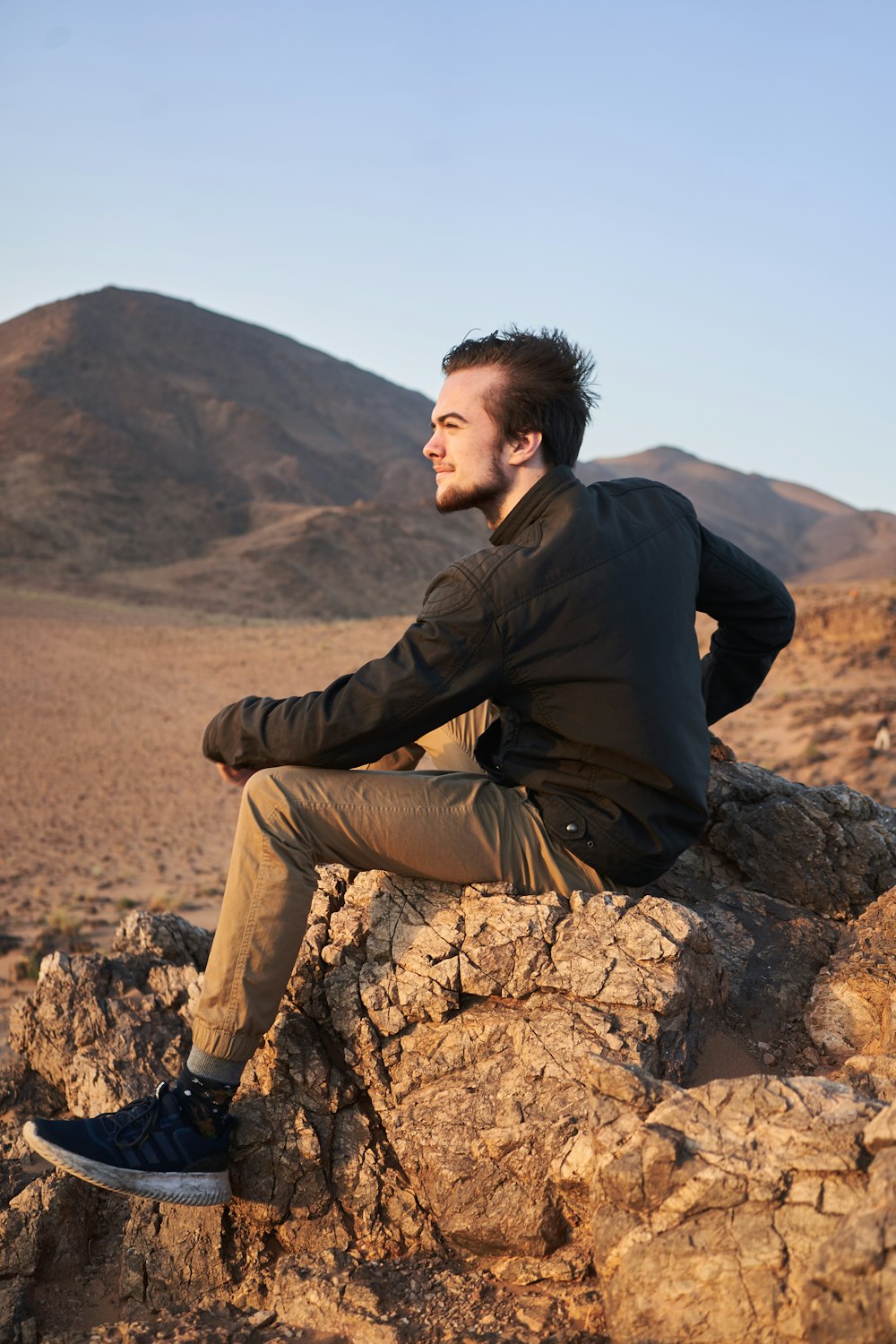 man wearing black jacket sitting on rock viewing mountain