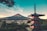 A traditional Japanese pagoda stands prominently in the foreground with Mount Fuji majestically rising in the background under a clear blue sky. The town below the mountain is nestled amidst lush greenery, suggesting a serene and peaceful atmosphere.