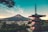 A traditional Japanese pagoda stands prominently in the foreground with Mount Fuji majestically rising in the background under a clear blue sky. The town below the mountain is nestled amidst lush greenery, suggesting a serene and peaceful atmosphere.