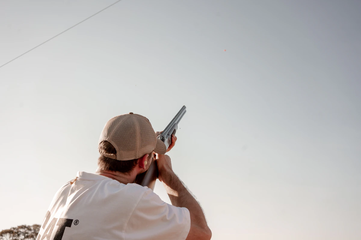 Shooter taking aim with a shotgun at a clay target