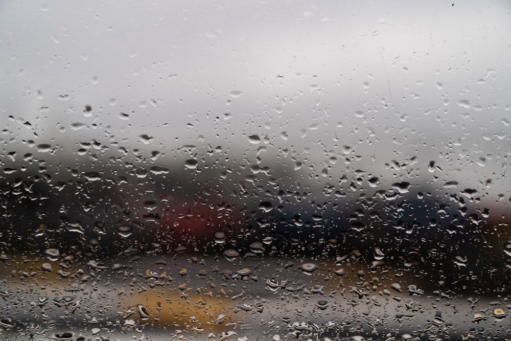 a rain covered window with a red car in the background