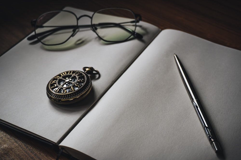 pocket watch, eyeglasses, and pen on blank opened book