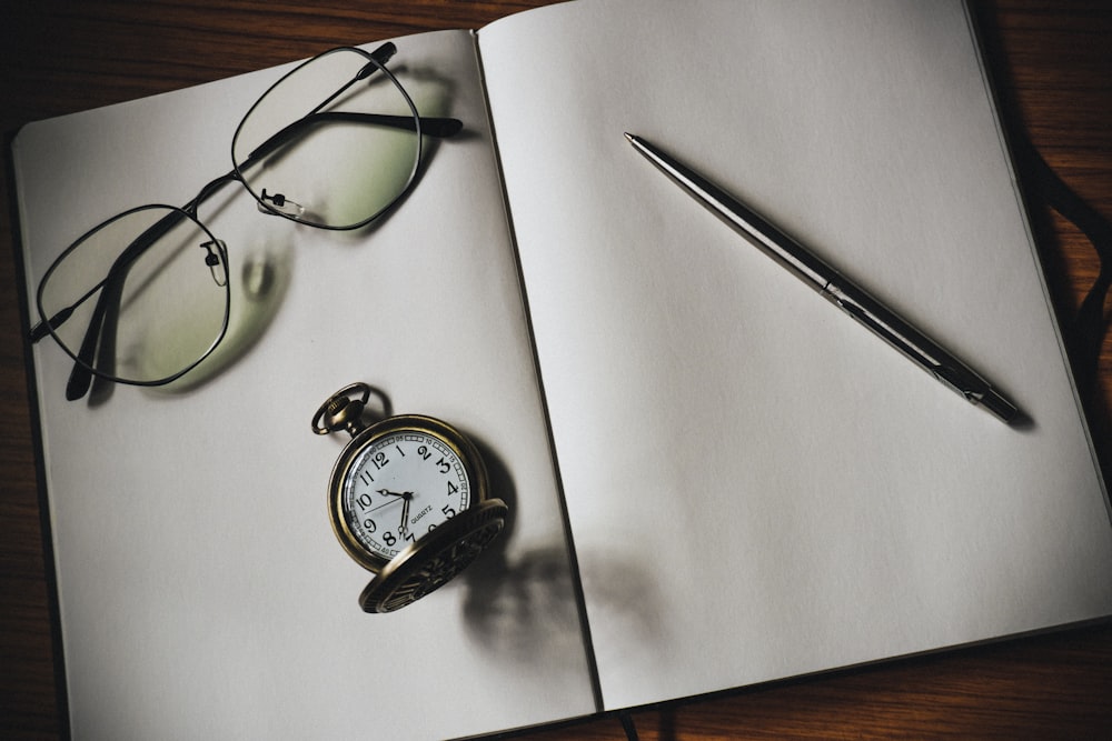 eyeglasses, pocketwatch, and pen on white blank notebook