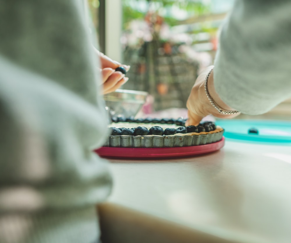 Person, die Blaubeere auf Blaubeer-Käsekuchen legt