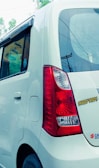 The rear side of a white car with a distinctive red tail light and an 'Angry Birds' sticker. The car window is partially open, revealing some signage inside. Electric poles and wires are visible in the background.