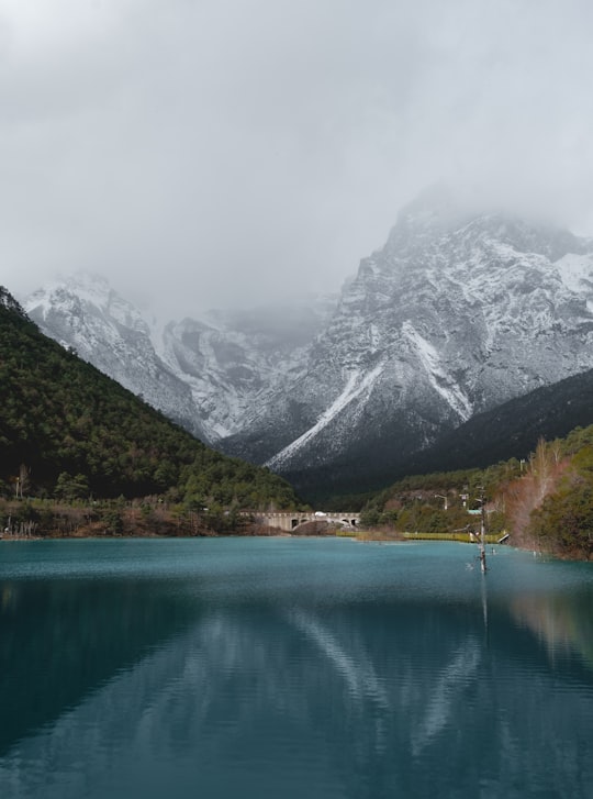 reflection of mountains and trees on body of water in Jade Dragon Snow Mountain China