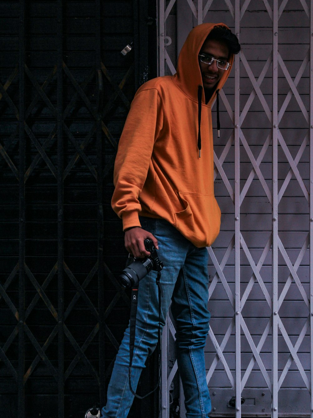 Hombre con sudadera con capucha naranja y jeans azules sosteniendo la cámara