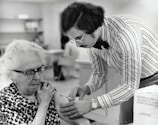 grayscale photography of man holding syringe injecting on woman left arm