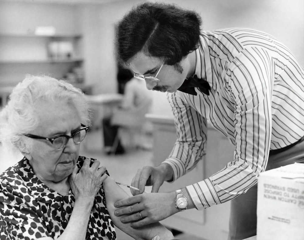 grayscale photography of man holding syringe injecting on woman left arm