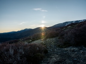 Sunset over Himalayan mountain peaks with lush valley below, viewed from a serene hilltop plot.