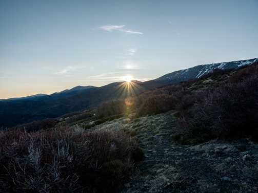 Sunset over Himalayan mountain peaks with lush valley below, viewed from a serene hilltop plot.