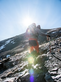 Hiker using navigation tools like a GPS and compass on a mountain trail during a bright day.
