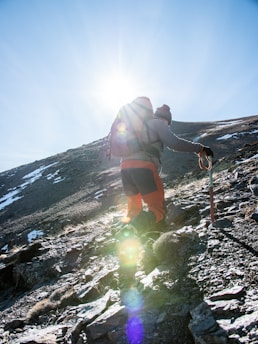 A determined hiker climbing a steep mountain trail under a bright sky