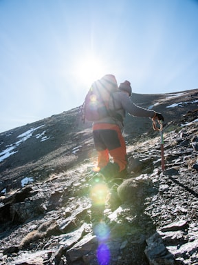 Hiker using navigation tools like a GPS and compass on a mountain trail during a bright day.