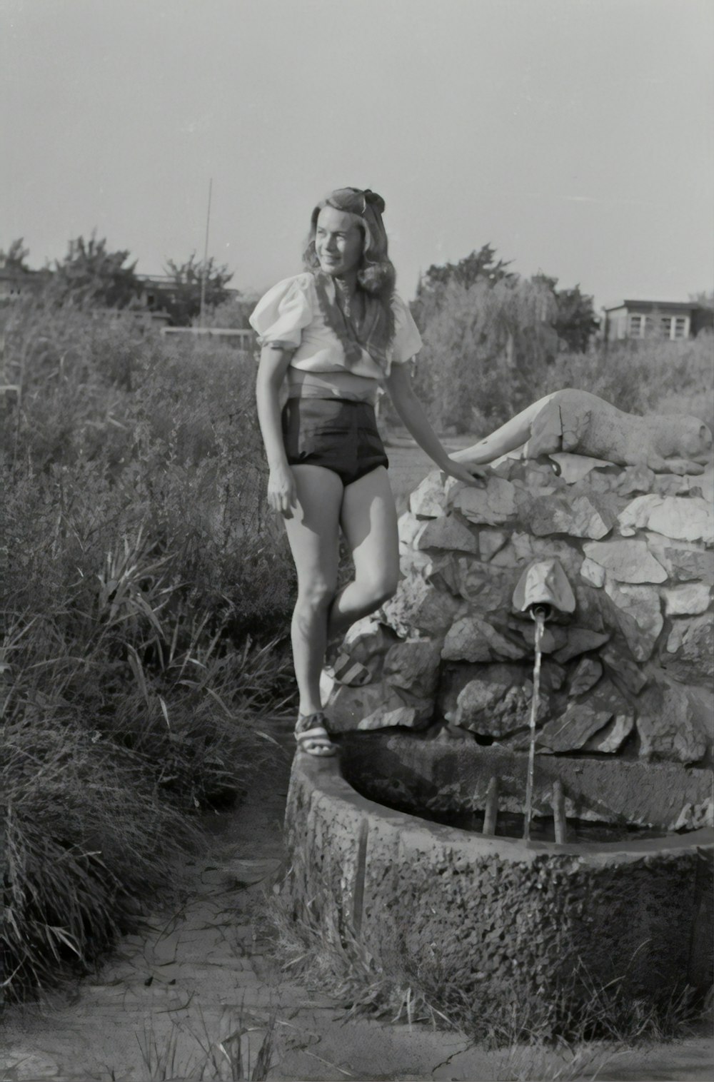 grayscale photography of woman standing near water well