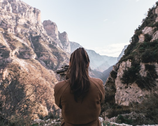 woman in brown sweater sitting on hill in Vikos Greece