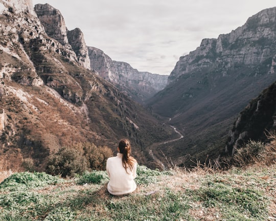 woman in white top sitting on hill in Vikos National Park Greece
