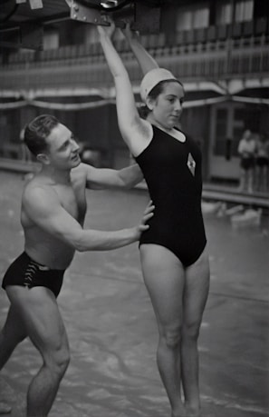 Instructors guiding a teen through an acrobatic partner pose in the gym.