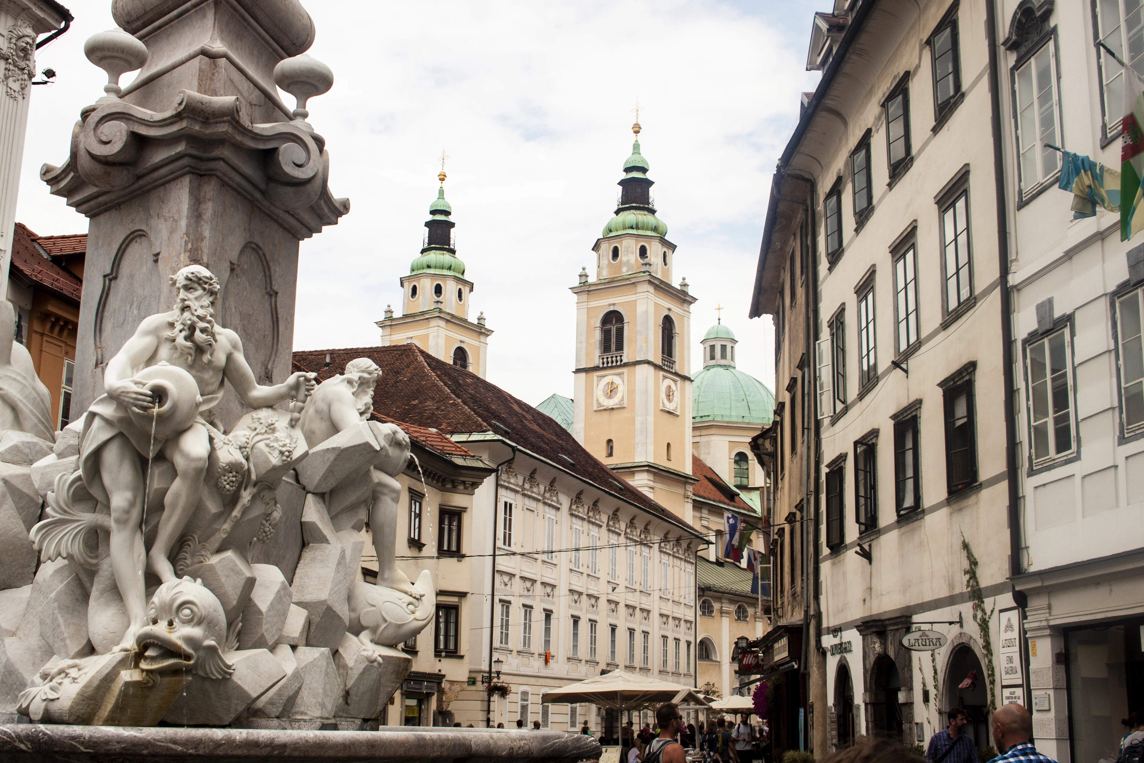 A baroque fountain on Ljubljana's town square with the cathedral's green domes rising behind
