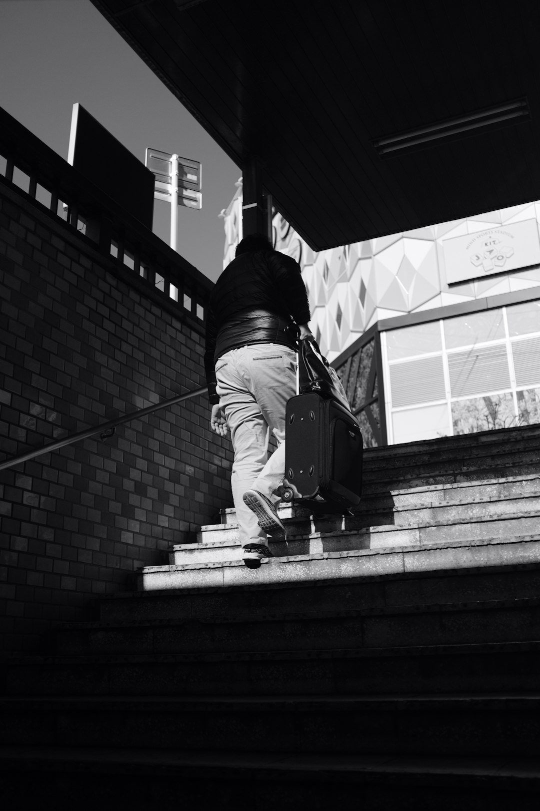 grayscale photography of person walking on stairway while carrying luggage during daytime
