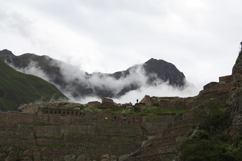 few people standing near brown castle viewing mountain under white sky